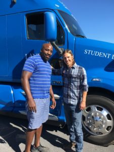 two men standing in front of blue semi truck smiling